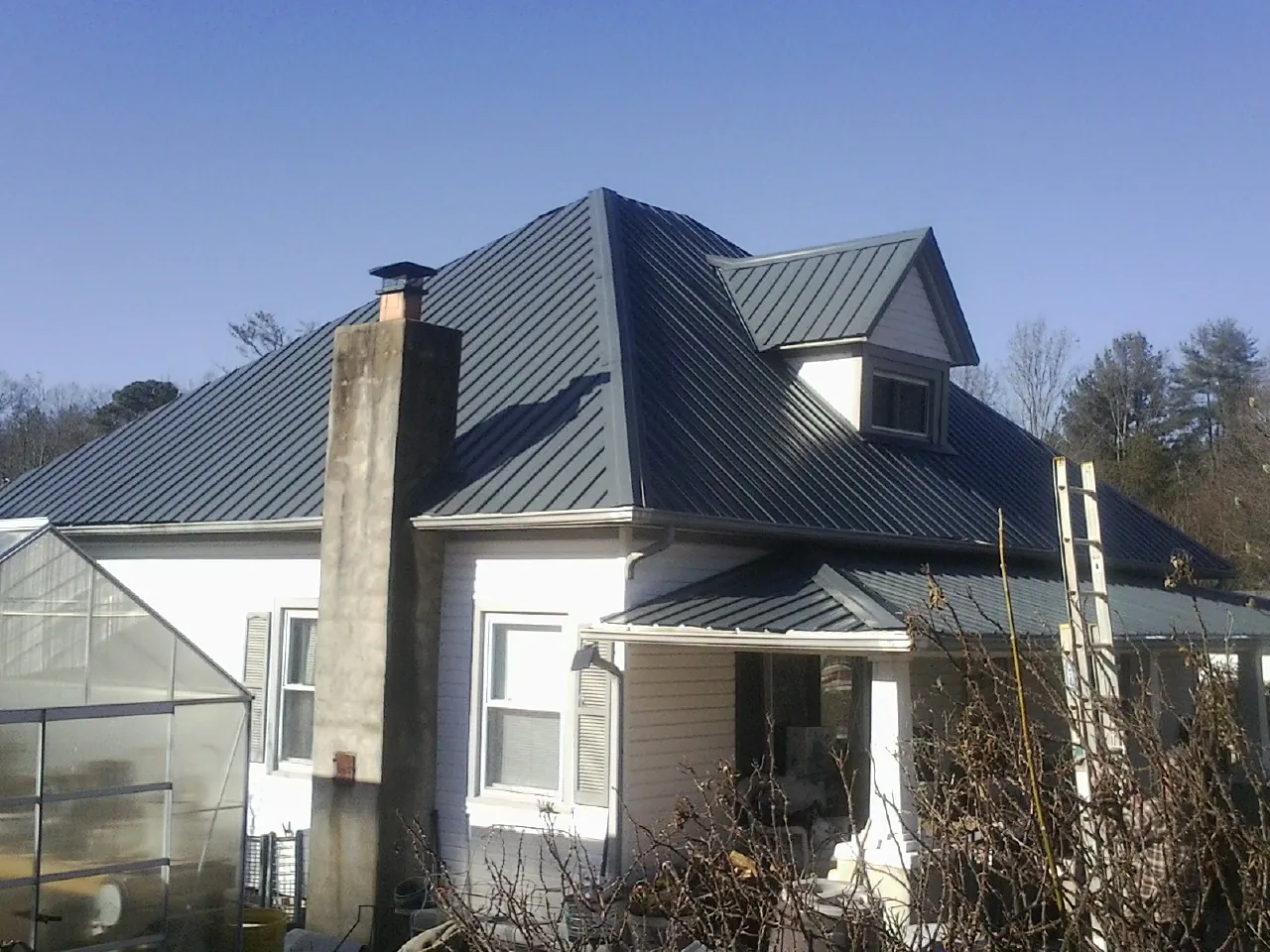 Dark blue standing seam metal roof on a white farmhouse with dormer — Slate & Tile Roof Repair by Roofing Brothers in Shoshone
