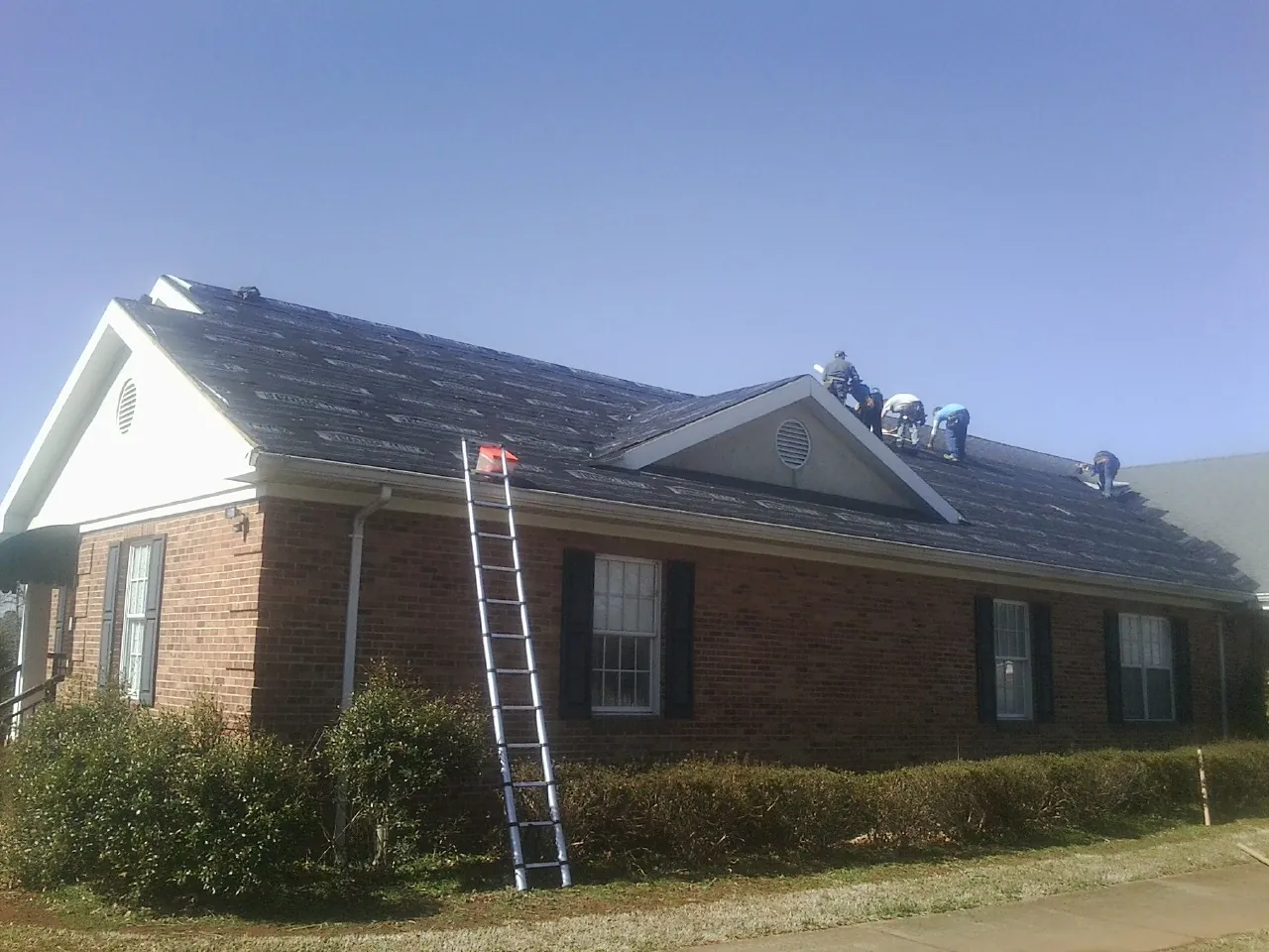 Crew tearing shingles off a brick ranch roof with a ladder set — Metal Roof Repair work by our crew in Shoshone