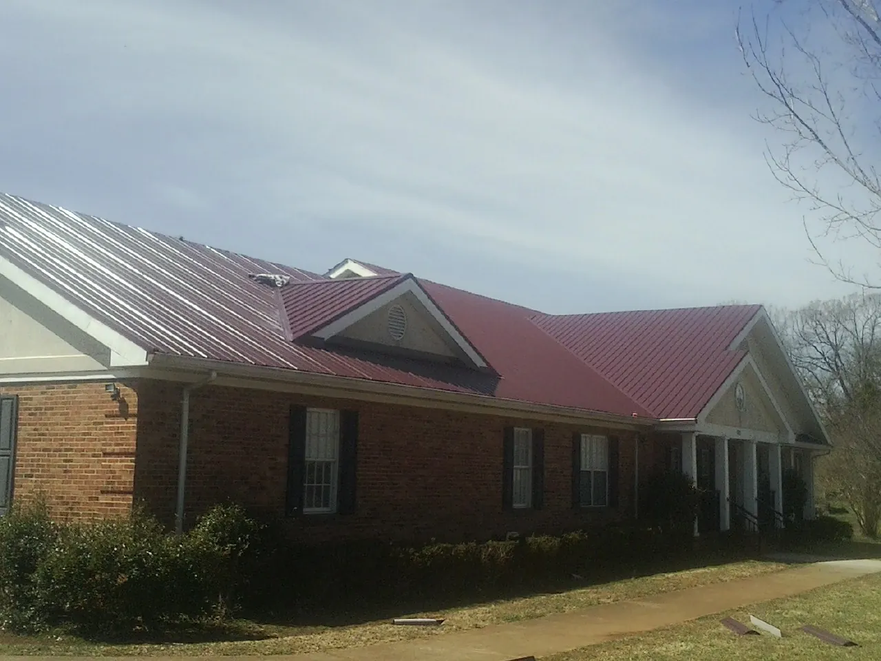 Red metal roof with gabled entries on a long brick building, from a Hail Damage Roof Repair job in Shoshone