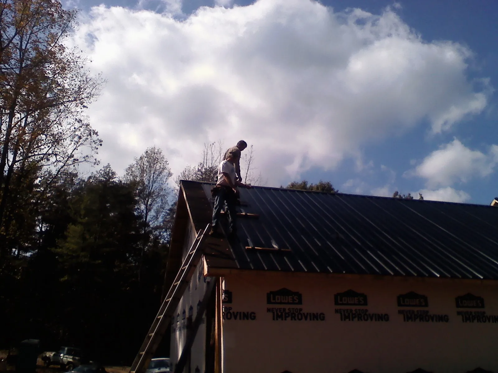 Roofer fastening dark metal panels high against a cloudy sky, from a Roof Inspection job in Shoshone