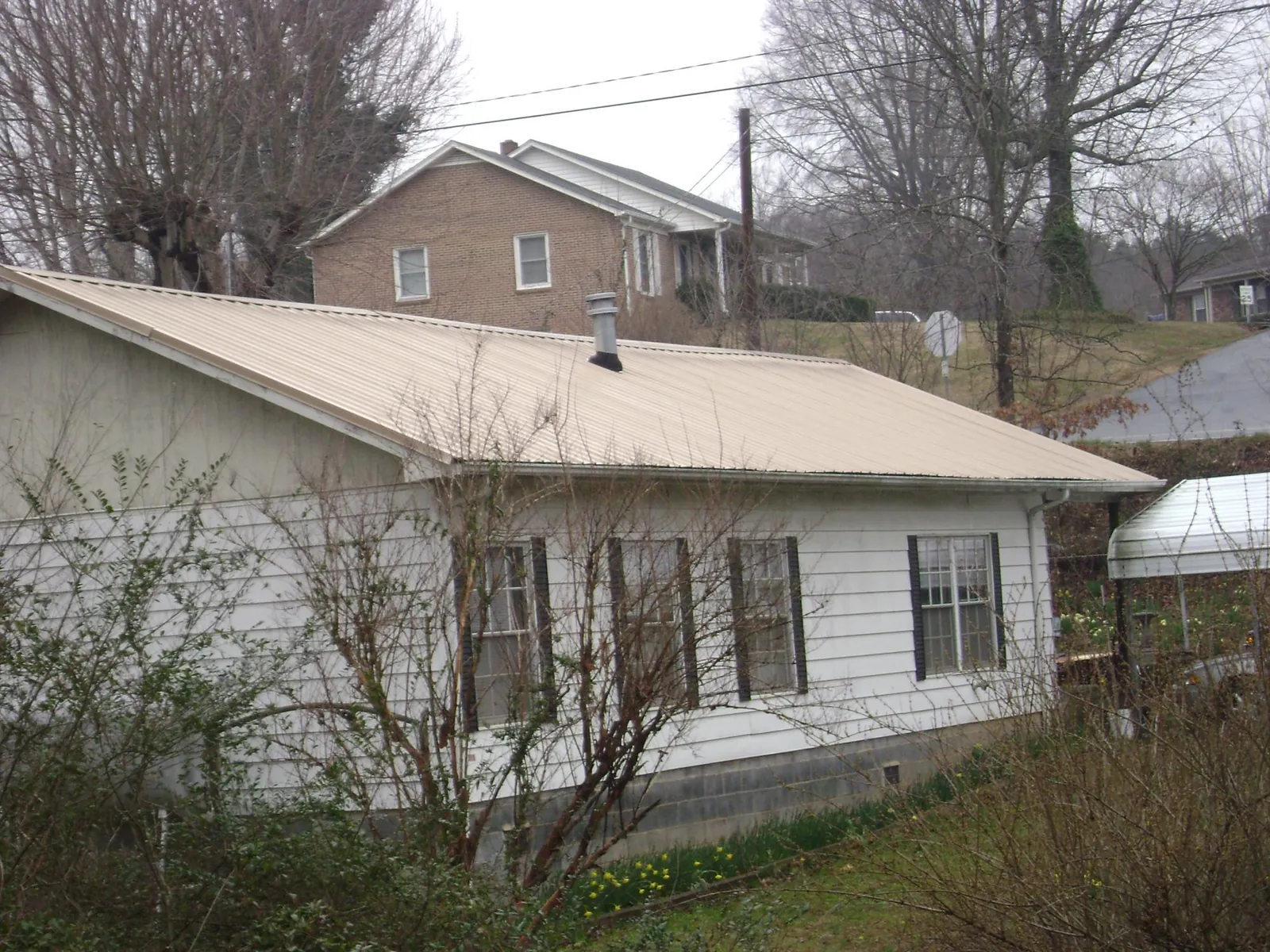 Tan metal roof on a white sided house set into a hillside — Commercial Roofing by Roofing Brothers in Shoshone